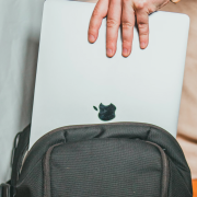 A person’s hand places a silver laptop with a visible Apple logo into the main compartment of a black backpack, turning it into a sleek Mobile Design Studio on the go.